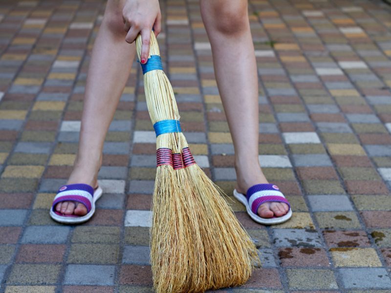 Little Girl Sweeping Cobblestone Floor Using Straw Broom