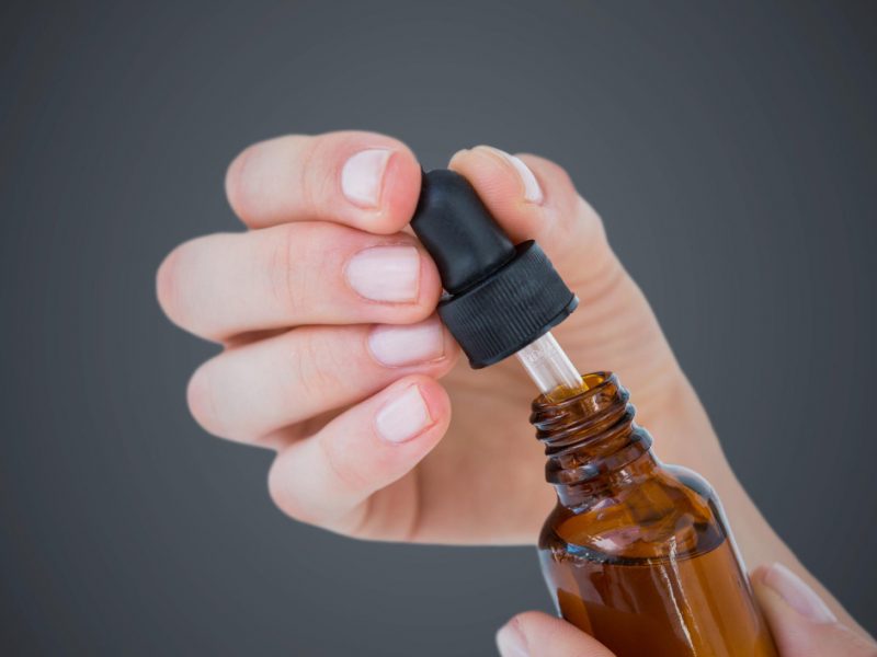Hand With Dropper Bottle Against Grey Background