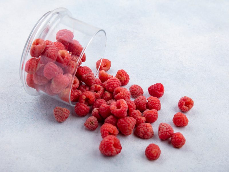 Side View Raspberries Spilling Out Glass Bowl White