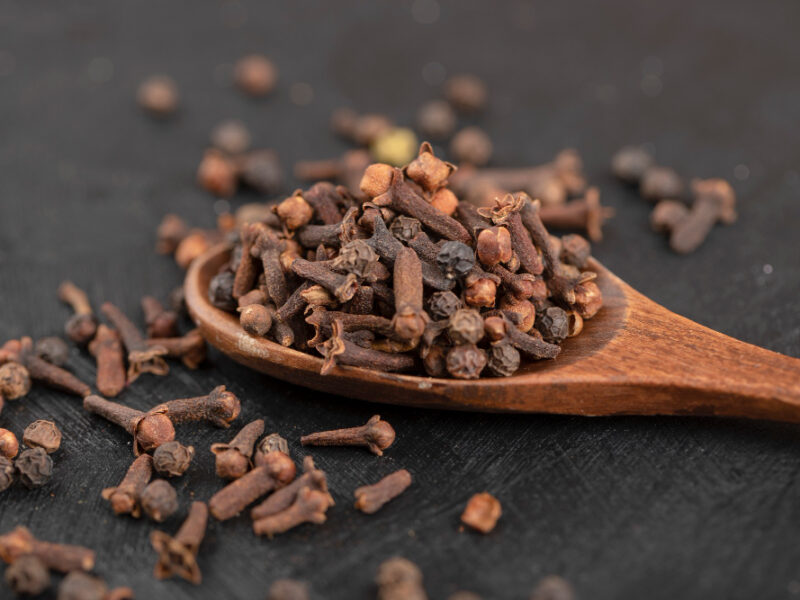 Pile Dried Natural Cloves With Wooden Spoon Black Surface