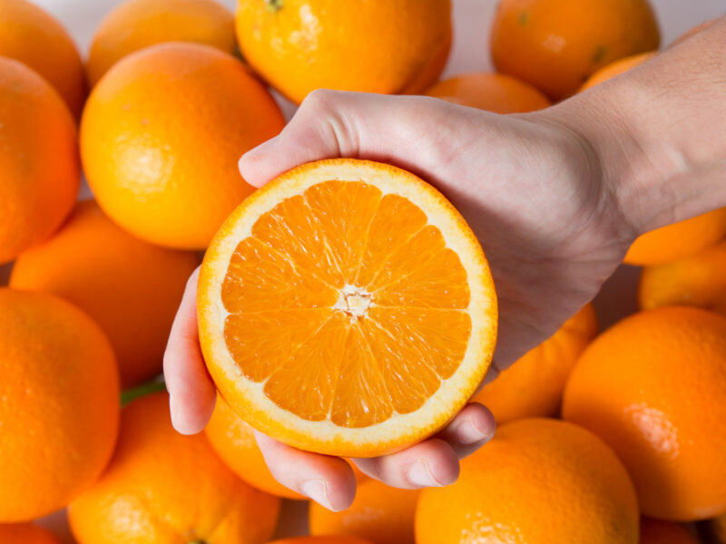 person-showing-cut-orange-half-pile-fruits