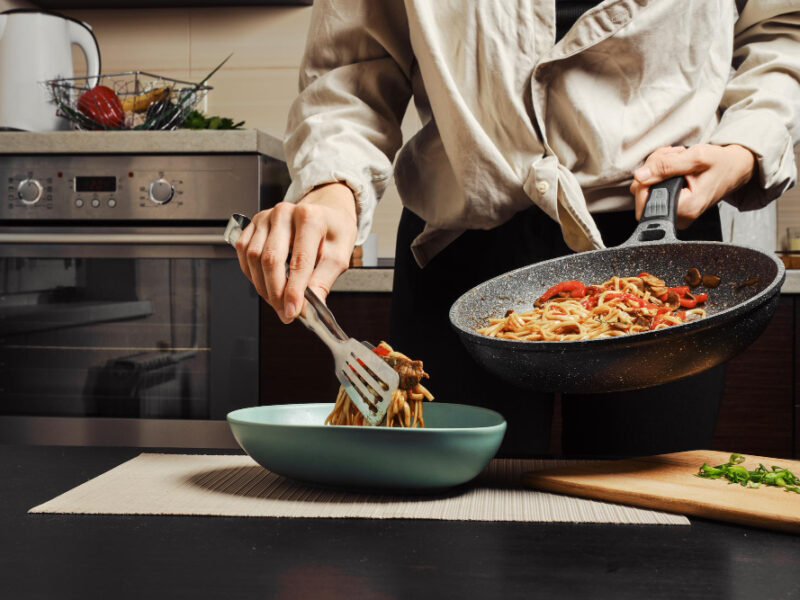 Unrecognizable Woman Moving Cooked Noodles With Vegetables Beef From Frying Pan Into Plate