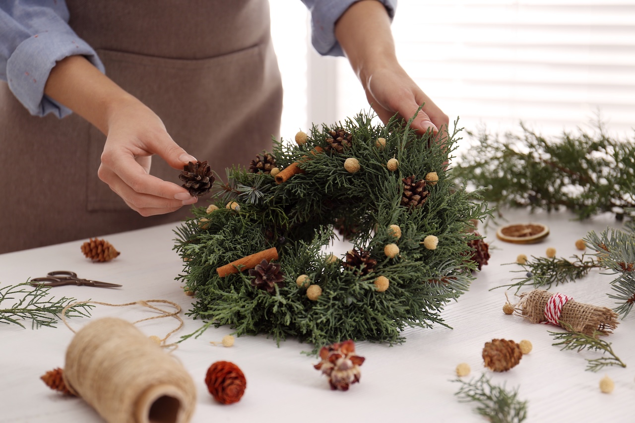 Florist Making Beautiful Christmas Wreath At White Wooden Table Indoors, Closeup