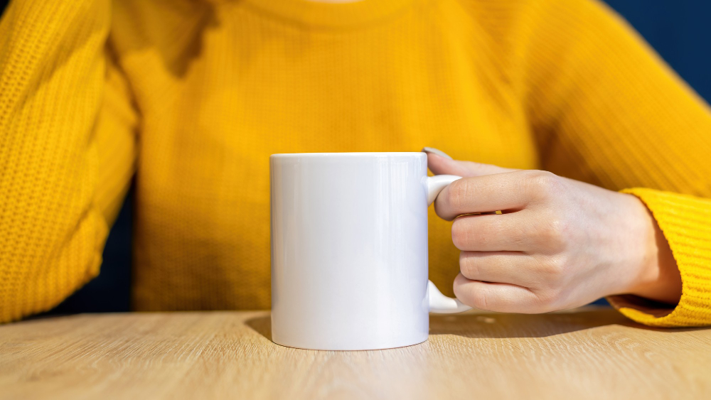 woman-sweater-holding-cup-wooden-table