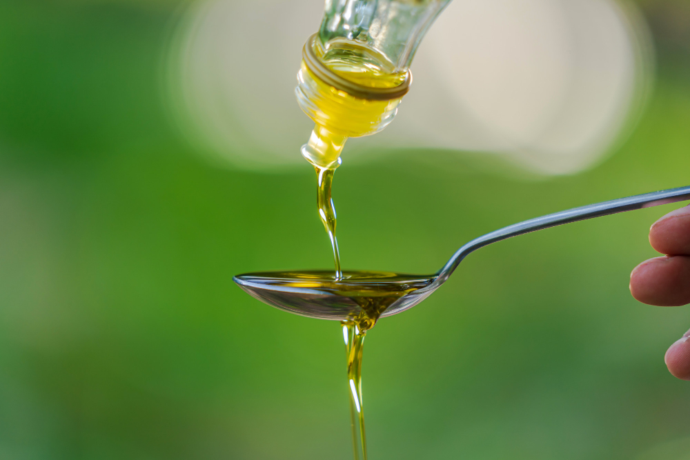 pouring-olive-oil-into-spoon-green-park-garden-background