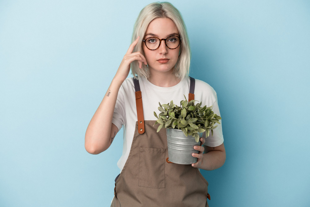 Young Gardener Caucasian Woman Holding Plant Isolated Blue Background Pointing Temple With Finger Thinking Focused Task